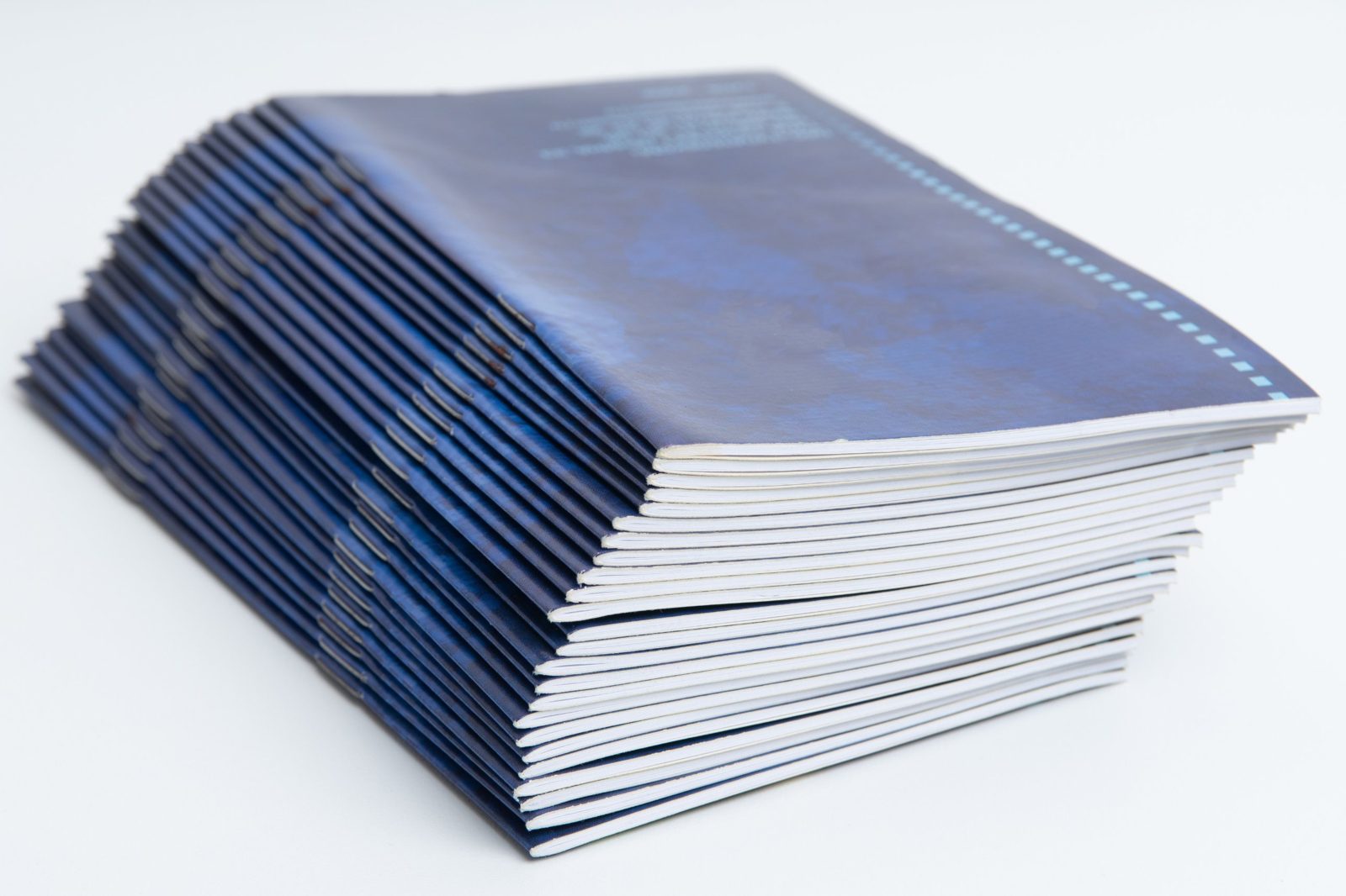 Stack of saddle-stitched booklets with staples visible along the folded spine